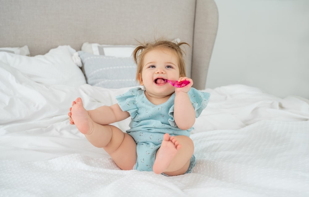 Baby girl sitting on bed playing with toothbrush