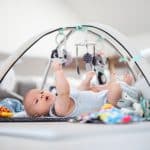 Cute baby boy playing with hanging toys arch on mat at home Baby activity and play center for early infant development. Best baby activity Center