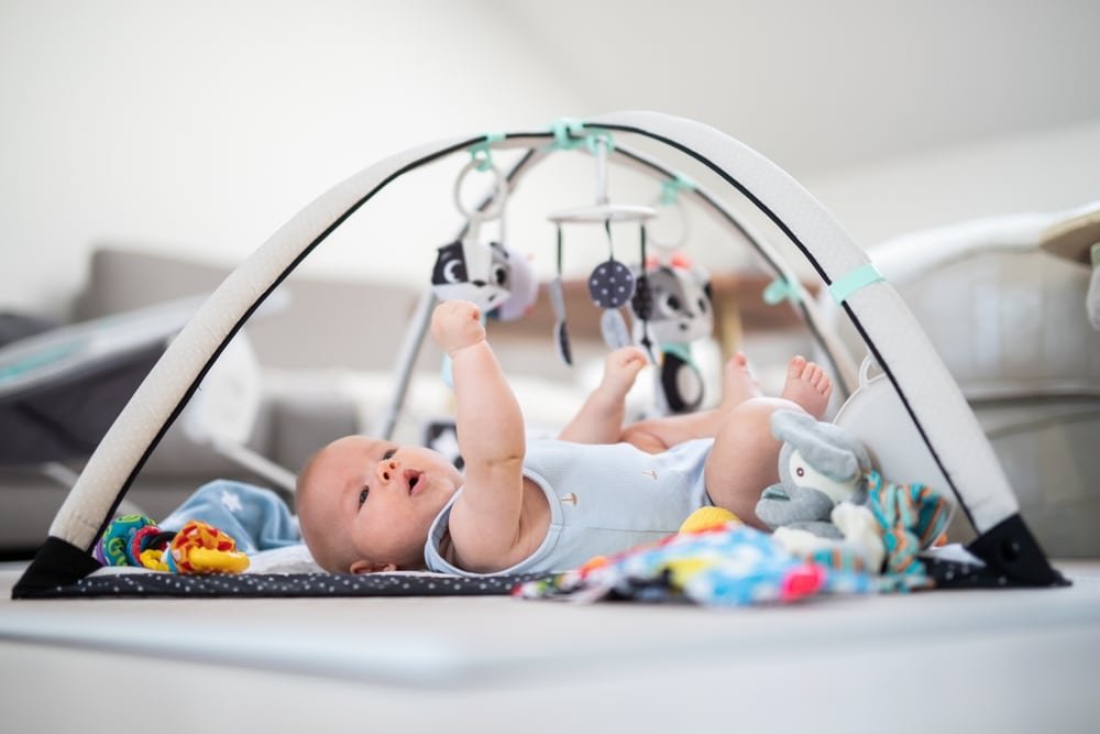 Cute baby boy playing with hanging toys arch on mat at home Baby activity and play center for early infant development. Best baby activity Center