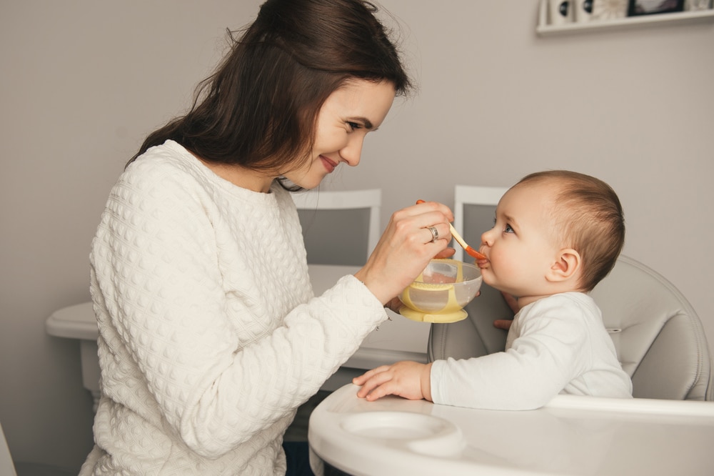 Mom feeding organic baby cereal her baby girl with a spoon