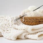 White balls of yarn in a wooden wicker basket on a white knitted blanket
