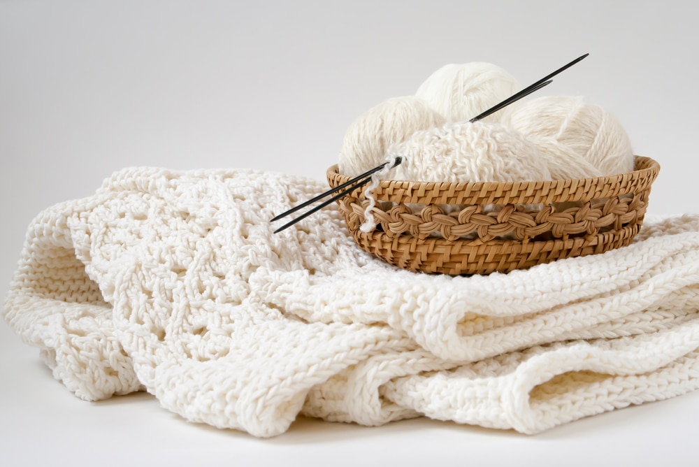 White balls of yarn in a wooden wicker basket on a white knitted blanket