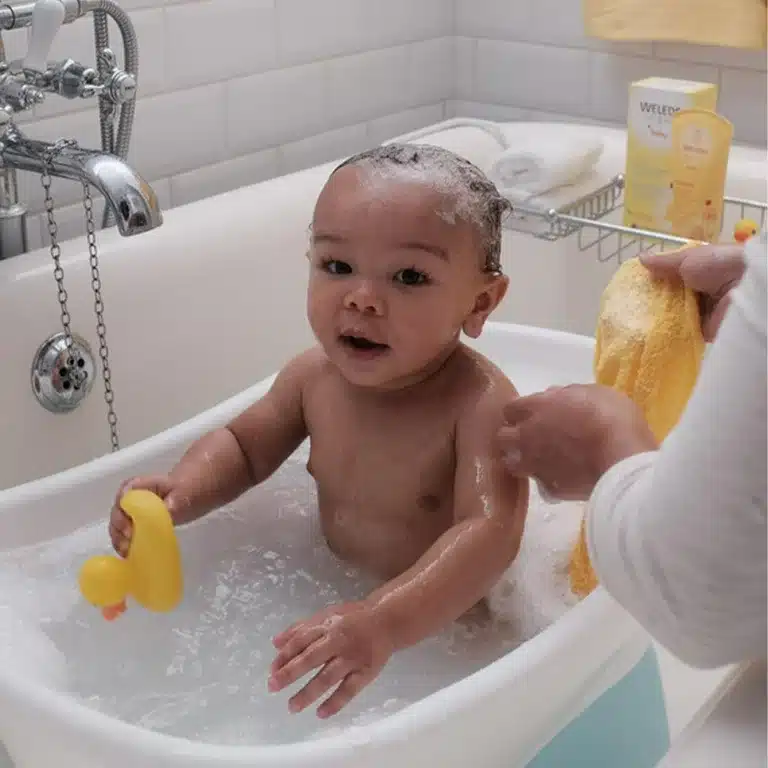 Baby sitting in a bathtub mom using Weleda Baby Calendula Shampoo Body Wash