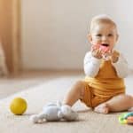 Portrait of smiling cute little child using colorful toys, chewing teether