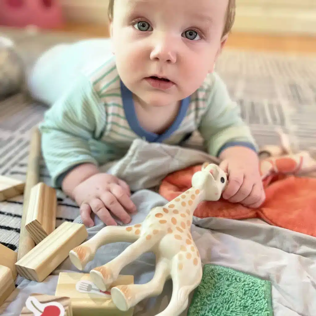 a baby lying on stomach and holding Sophie la Girafe​ teether