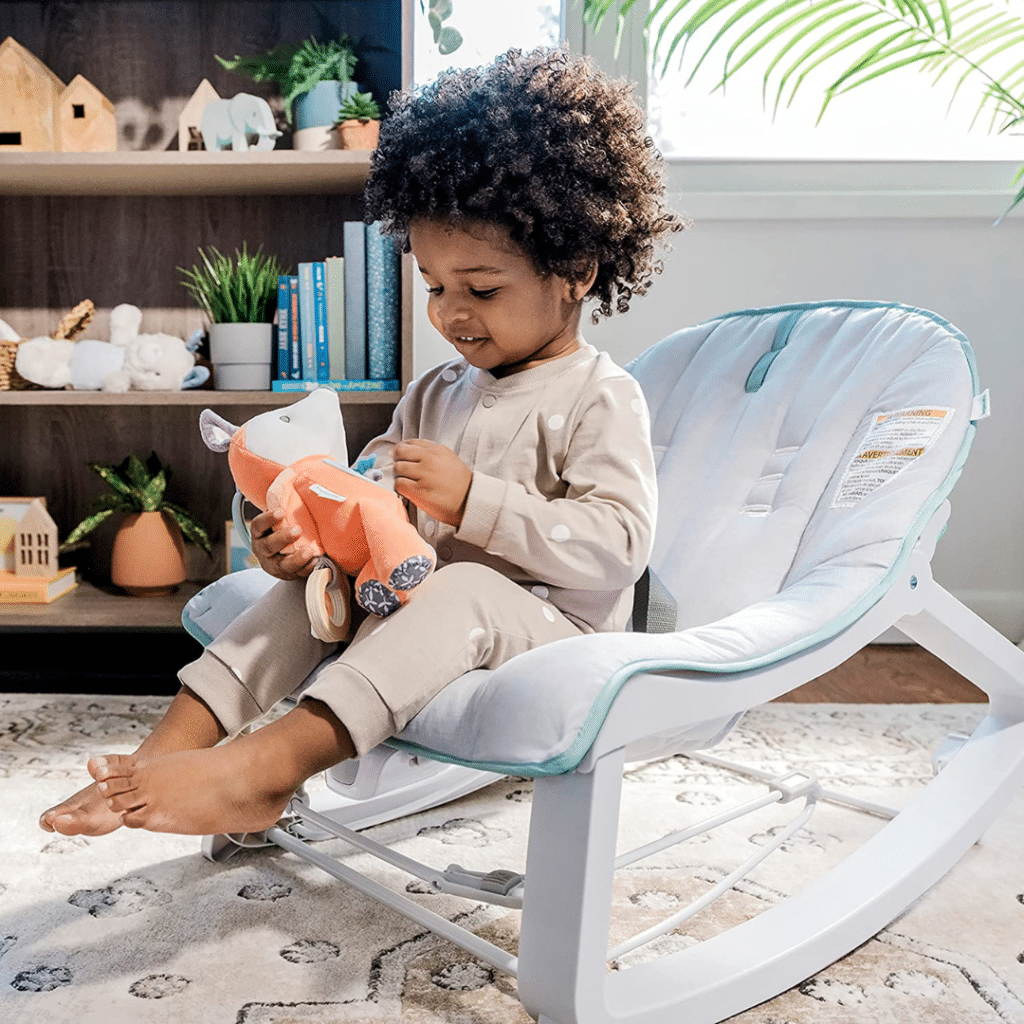 a baby playing with a toy relaxing in Ingenuity Keep Cozy in Bouncer