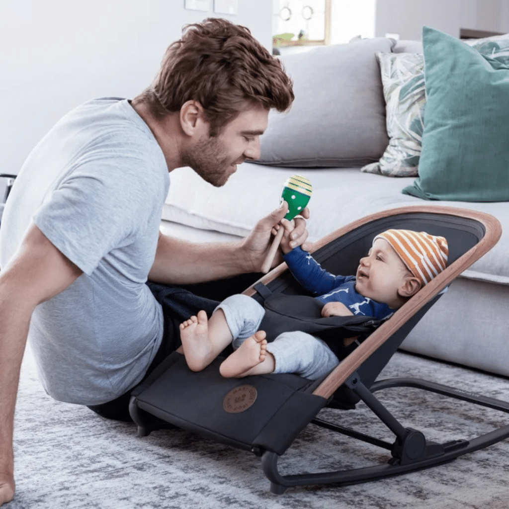 a dad playing with his baby lying in Maxi Cosi Kori in Baby Bouncer Seat
