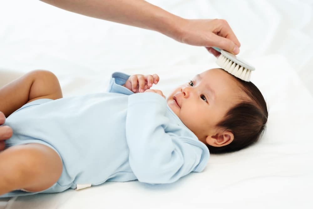 Mother Combing Her Newborn Baby Hair On A Bed
