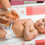 Mother makes massage for her baby and apply oil on the hands in child room at home