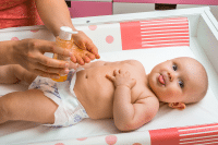 Mother makes massage for her baby and apply oil on the hands in child room at home