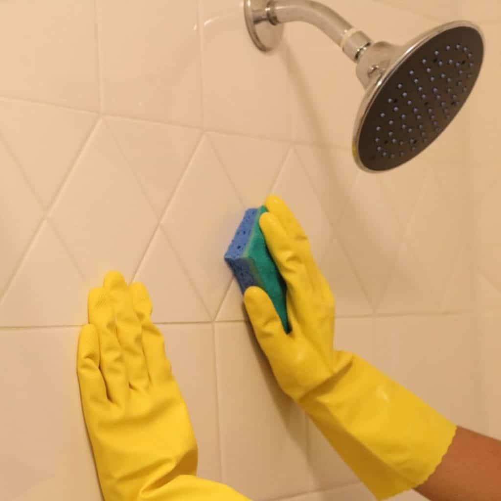 A vie wof rubber gloved hands scrubbing the shower wall