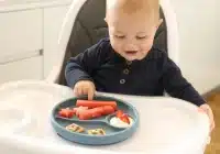 a baby eating food from grey colored divided plate