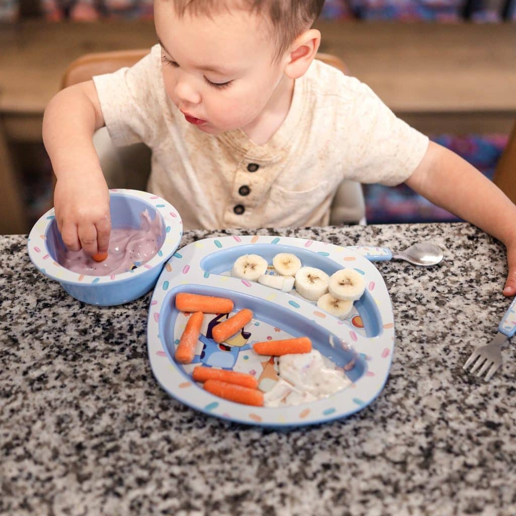 a toddler eating from The First Years Bluey Piece plate and bowl