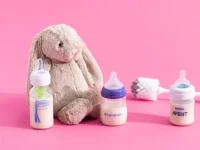 different baby bottles placed on a pink surface with a teddy