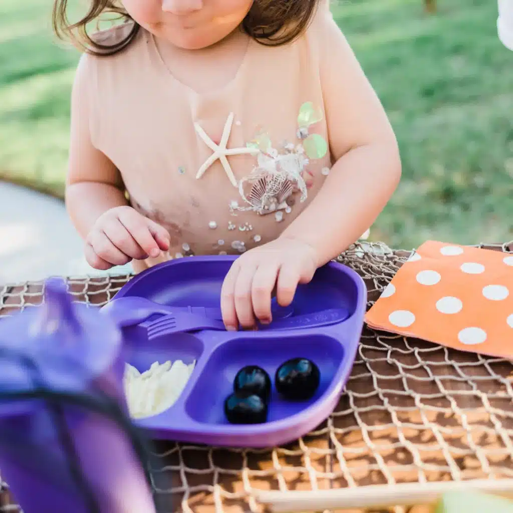 half view of a baby girl eating food from Re Play Toddler Plates with Dividers