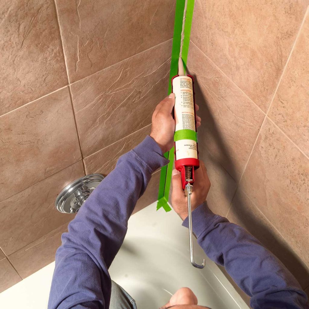A view of a person sealing a bathroom wall with caulk