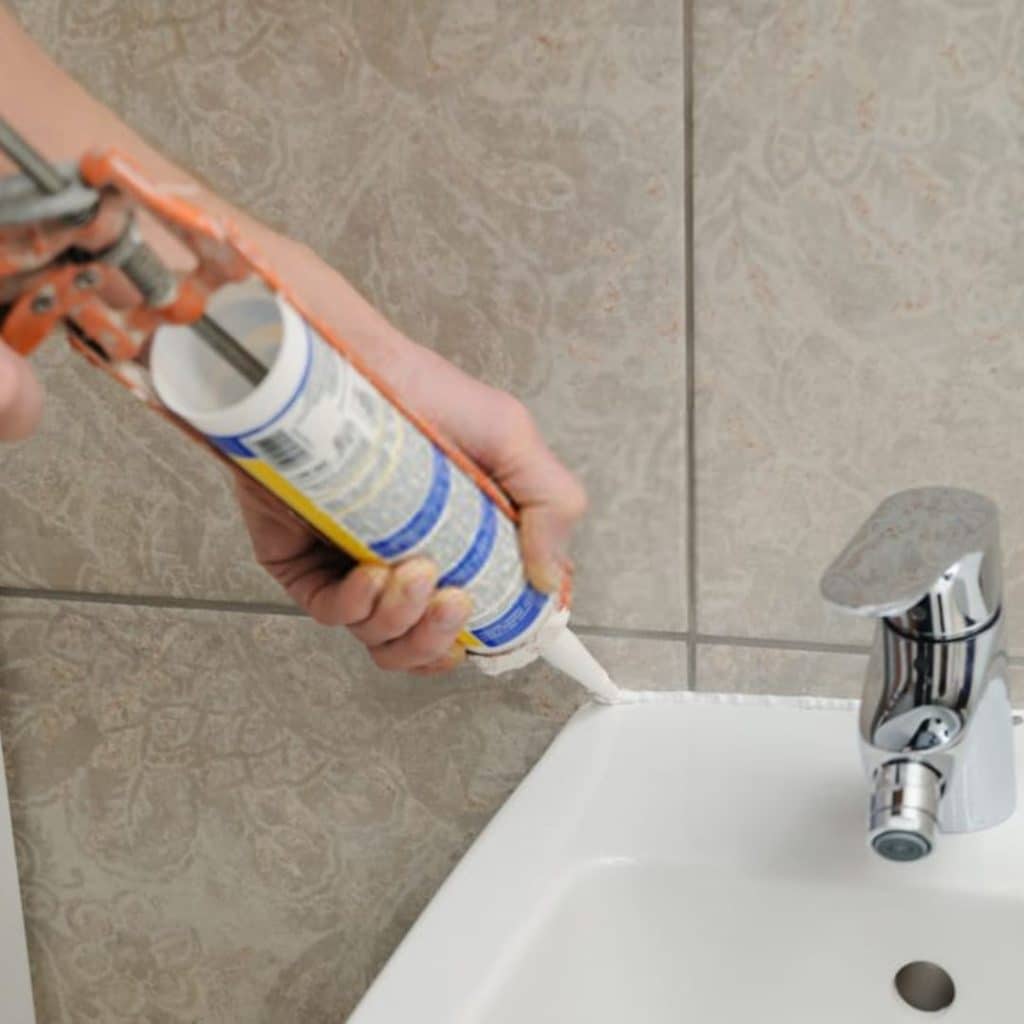 A view of a person holding a caulk to a bathroom sink