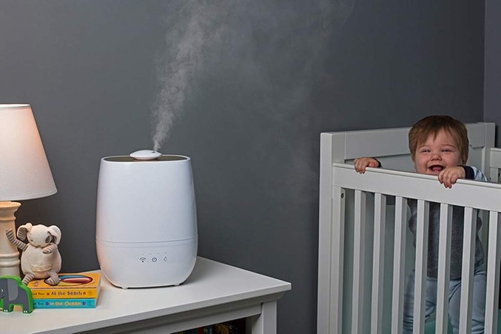 Baby sitting in a crib smiling humidifier placed on the side table