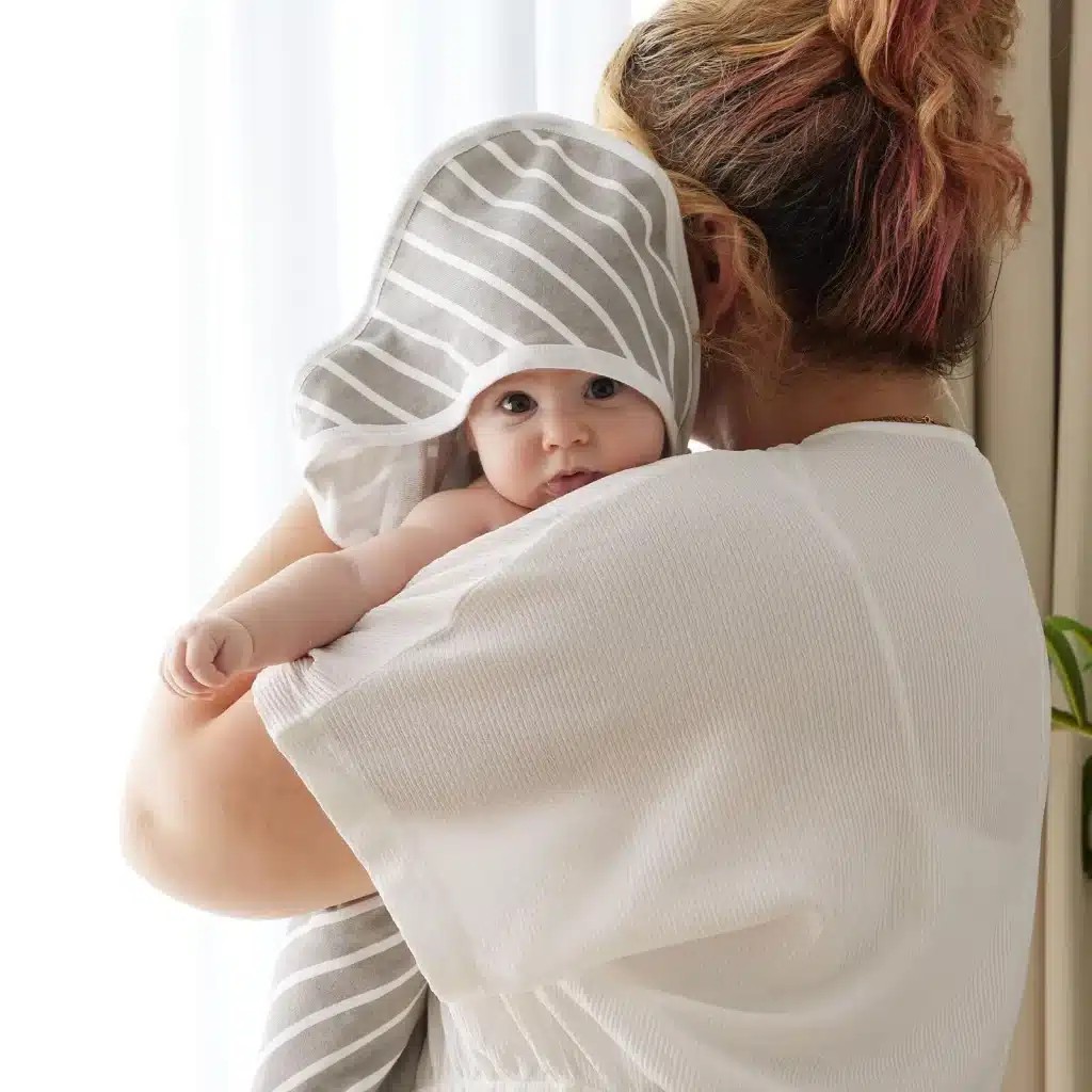 a mother holding a baby wrapped in Momcozy Baby Hooded Towel looking at the camera