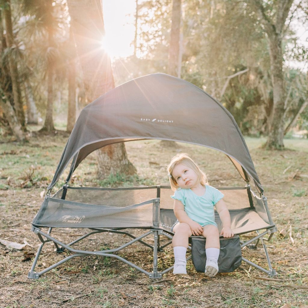 A baby girl sitting on Baby Delight Go with Me Deluxe Portable Cot