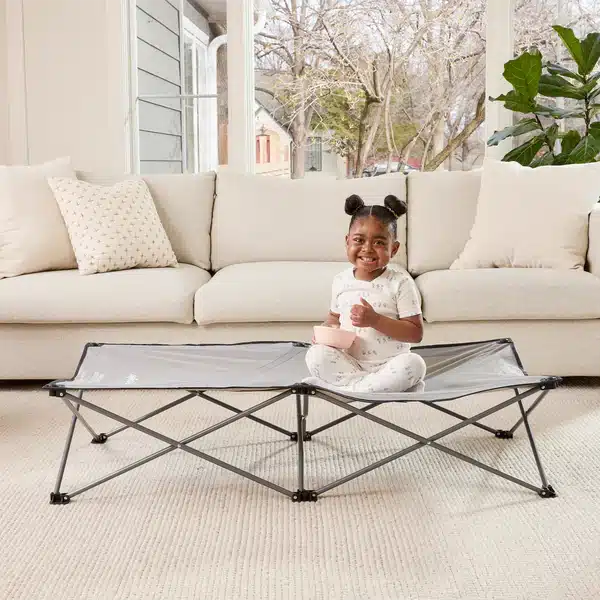 a baby girl sitting on Regalo Extra Long My Cot Portable Toddler Bed