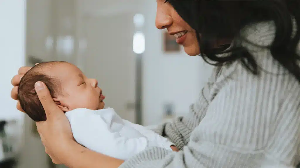 Smiling woman gently holding a sleeping newborn baby in her arms