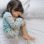 a baby girl holding her tummy due to stomach pain and lying on bed