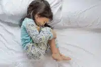 a baby girl holding her tummy due to stomach pain and lying on bed