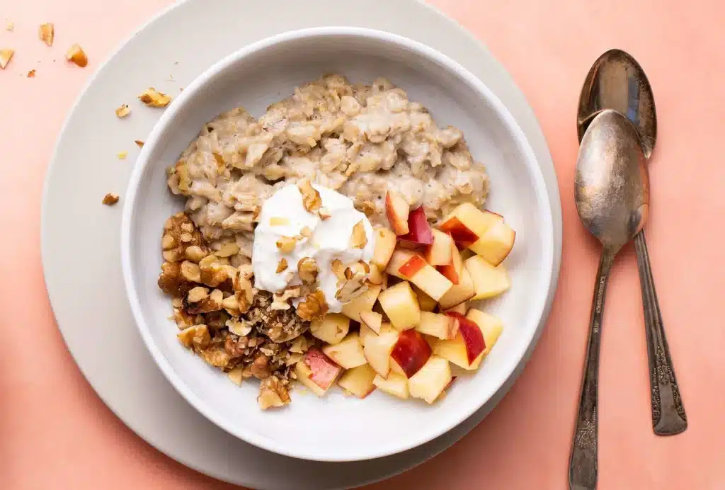 a bowl of oatmeal with fruits and nuts with - spoons on side
