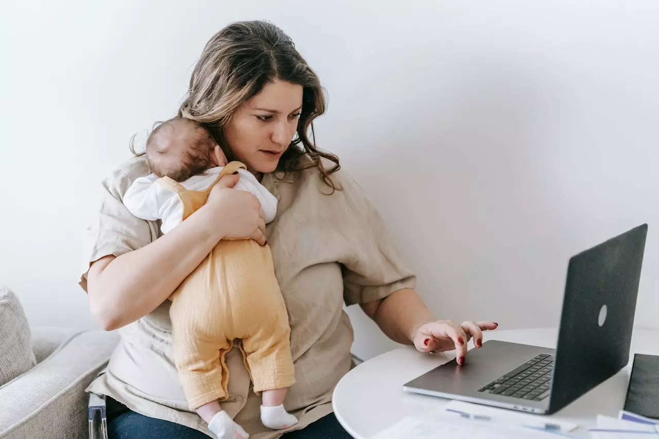 a mom holding her baby working on a laptop