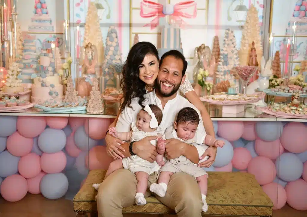 a new mom and dad with their twin babies party decor in the background