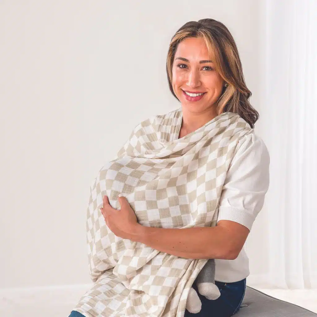 a new mom smiling looking at the camera holding baby under a nursing cover